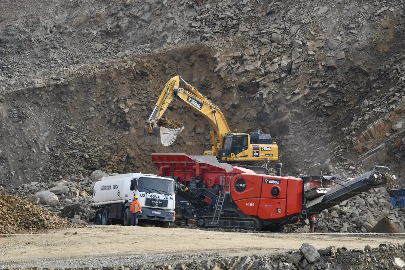 Bagr nakládá materiál do mobilního drtiče ve stěně lomu